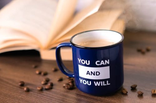 Inspirational coffee moment with a motivational quote on a mug beside an open book.